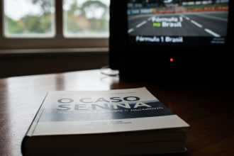 Livro 'O Caso Senna' em destaque, com F1 ao fundo